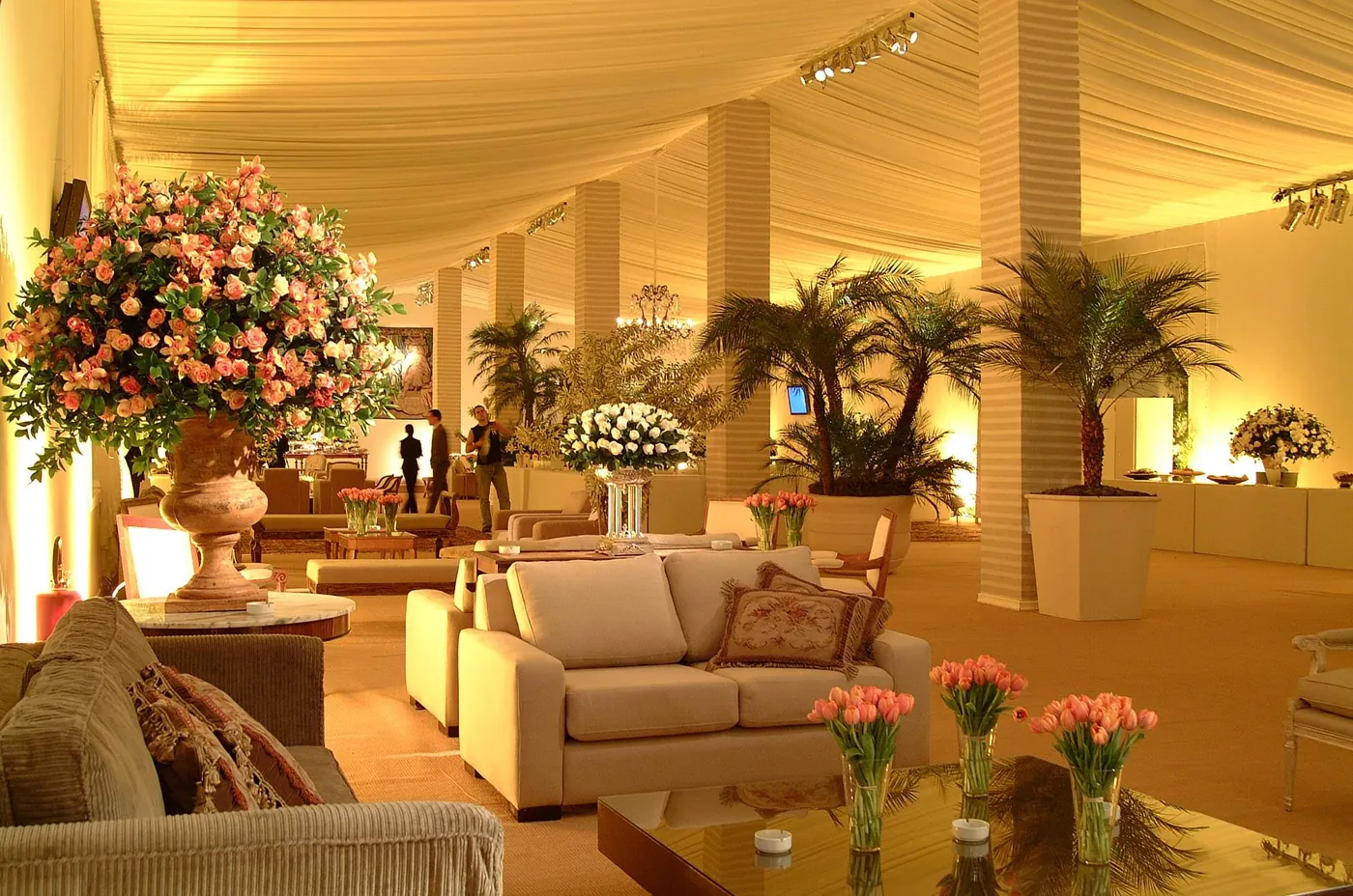 Lounge com sofás claros e arranjos de rosas sob luz quente