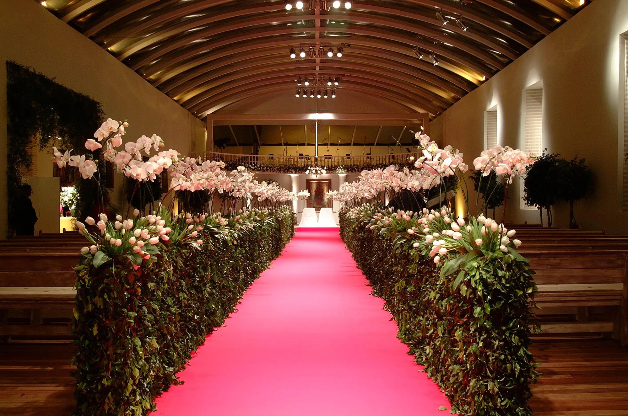 Corredor de igreja com tapete rosa e arranjos de orquídeas