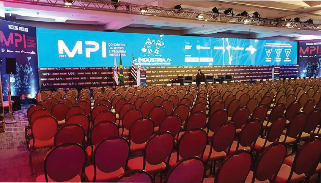 Plenária com cadeiras vermelhas diante de painel de LED