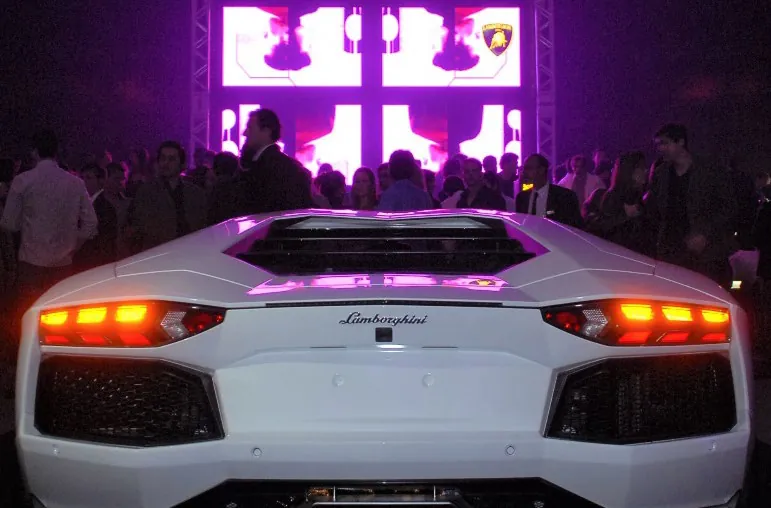 Lamborghini Aventador branco sob luz roxa, com convidados ao fundo